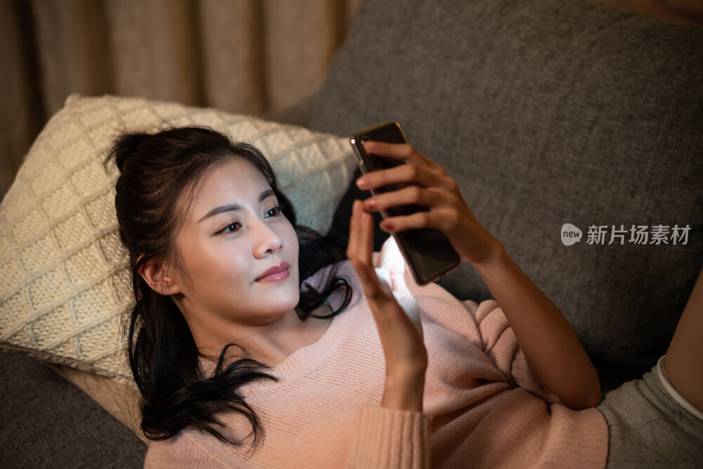 年轻女士躺在沙发上玩手机