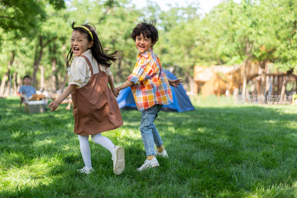 两个孩子在草地上手拉手开心奔跑回头看